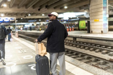 Man standing on a train station platform with his luggage, waiting for his train, embodying travel,