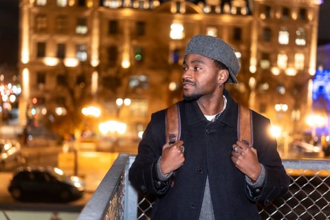 Young man in a beret and coat with backpack pauses on an illuminated paris street at night, gazing