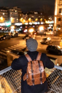 Person with a stylish leather backpack and knit cap viewing the illuminated cityscape of paris,