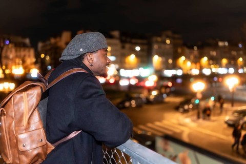 Young black man smiling and enjoying a stunning view of paris street lights at night, wearing a cap