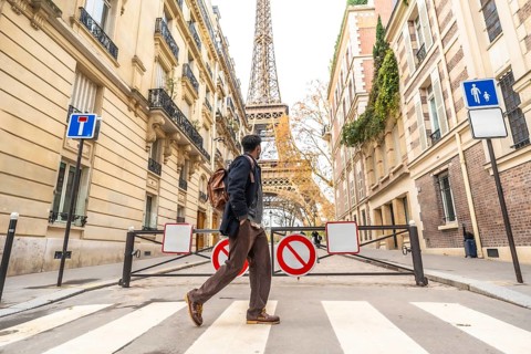 Young man with a backpack walking across a parisian crosswalk, historic buildings and the eiffel