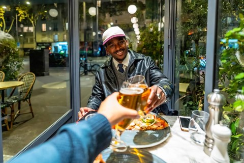 Young man smiling and feeling happy while toasting beer glasses with a friend during an evening
