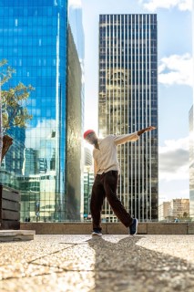 Young man with a red beanie striking a dynamic pose while dancing in an urban cityscape, backlit by