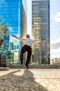 Young black man jumps with arms wide, celebrating joy and freedom against modern skyscrapers and