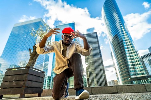 Young man wearing a red beanie and glasses, posing with hands raised in a low angle shot,