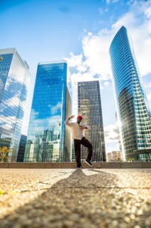 Black man striking a dynamic pose while dancing outdoors in a modern commercial district with glass