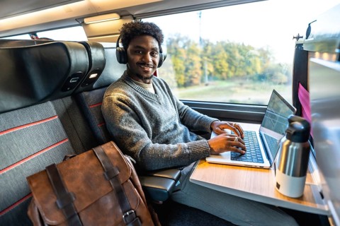 Young african man smiling, wearing headphones and typing on a laptop, working remotely or commuting