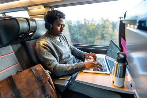 African man traveling on a modern train, wearing headphones and concentrating on his laptop,