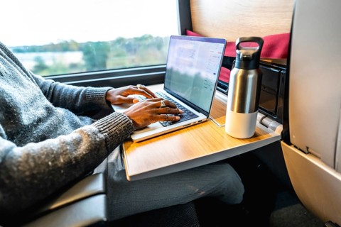 Man typing on a laptop computer while traveling by train, using the fold down tray table as a