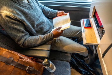Black man enjoying a book while traveling by train, reflecting concepts of leisure, modern