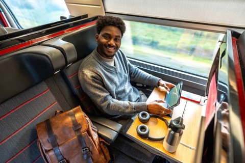 Young african american man traveling in a modern train, smiling and looking at the camera while