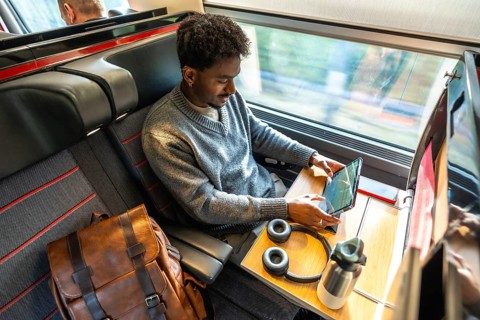 Young man traveling by high speed train, staying productive by working on a digital tablet at his