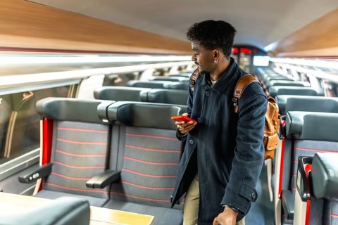 Young male passenger in a modern train carriage looking for his seat while checking travel