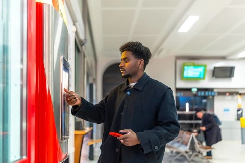 Young businessman standing at a train station, purchasing a ticket from an automatic vending