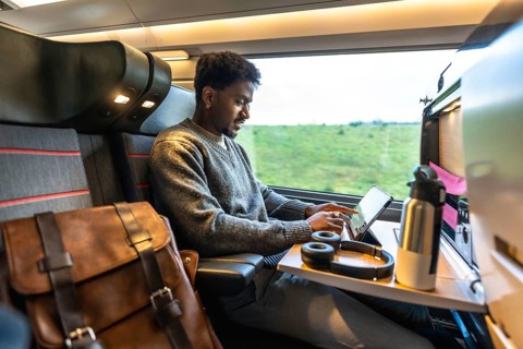Young african businessman staying productive on a train, working on a tablet with headphones,