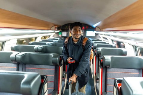 Young black man confidently walking through a train carriage, holding luggage and a mobile phone,