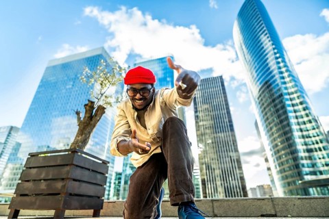 Happy young man wearing a red beanie and glasses, smiling and gesturing towards the camera,