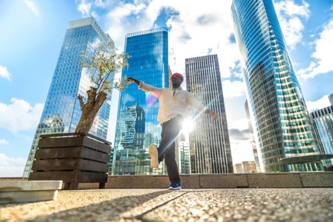 African american man dancing joyfully in a modern city square, arms outstretched against towering