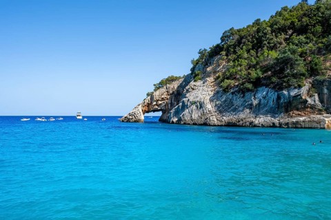 Light blue clear sea on a dream beach on Cala GoloritzÃ©, picturesque rocky coast with rock tunnel,