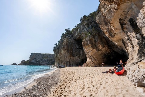Sandy beach beach and steep cliffs with caves at Cala Luna, Golfo di Orosei, Baunei, Sardinia,