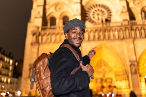 Joyful african american man with a backpack smiling and pointing, experiencing a nighttime tour of