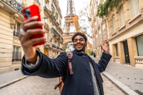 Young black man tourist smiling and recording a video selfie on his phone, waving hand, standing on