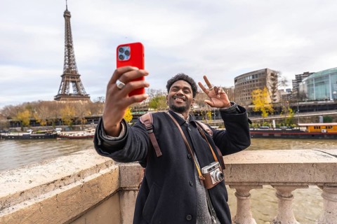 Young man smiling and making a peace sign while taking a selfie with a smartphone, capturing his