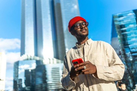 Young black man wearing a red beanie and glasses, smiling and looking up while holding a red