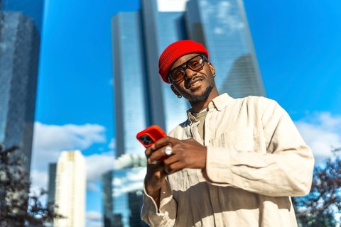 Young black man standing outdoors in a vibrant urban environment, smiling at the camera while