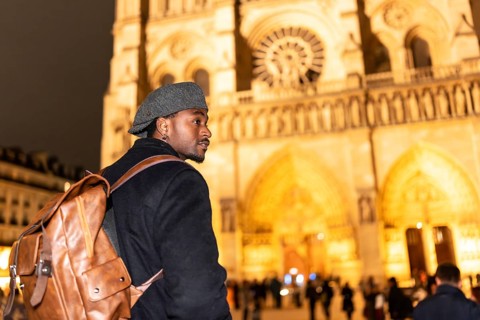 Young black man with a backpack and flat cap looking out while walking in front of notre dame