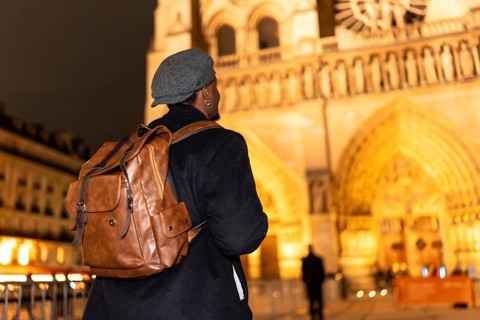 Solo man wearing a stylish cap and backpack, walking as a tourist during the night and looking at