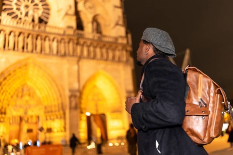Young man traveler with a backpack looking up at the majestic gothic architecture of notre dame