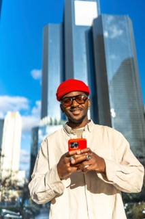 Stylish young black man wearing a red beanie and sunglasses, holding a bright red smartphone and
