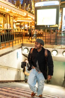 Young man wearing a beret, coat, and backpack ascending metro stairs in the vibrant urban