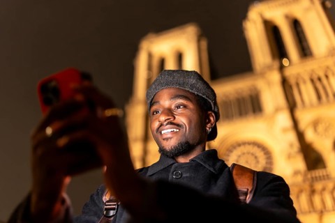 Young man enjoying a night street experience in paris, france, holding a smartphone and smiling