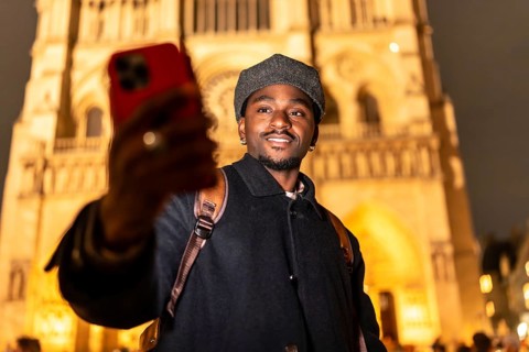 Young black man with a backpack smiling and taking a selfie with his smartphone in front of the