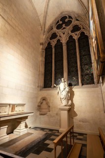 Gothic chapel interior featuring a statue of a saint, an arched window with detailed tracery, and