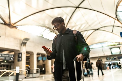 Indian businessman standing in a modern train station or airport terminal, looking down at his