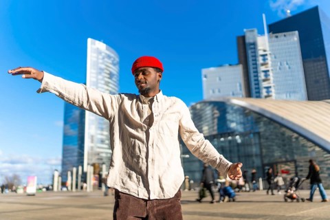 Black man wearing a red beanie and light shirt expressing creativity through dancing, arms spread