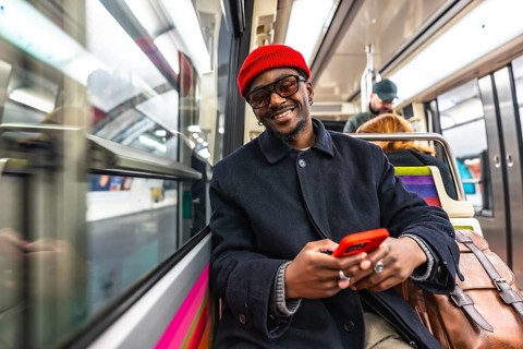 Young man smiling directly at the camera while holding and using a red smartphone, sitting on a