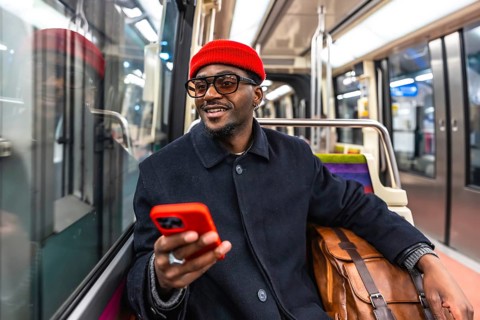 Young smiling african american man in a stylish coat and red beanie sits on a city train, holding a