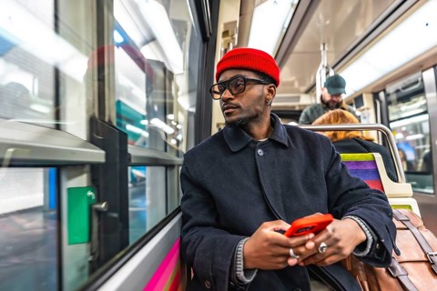 Stylish young black man wearing a red beanie and glasses sitting on a public transport train,