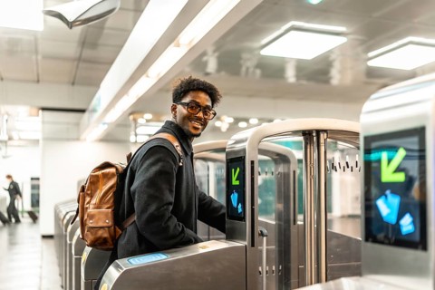 Young african american man with a backpack smiling, entering through a modern turnstile at a metro