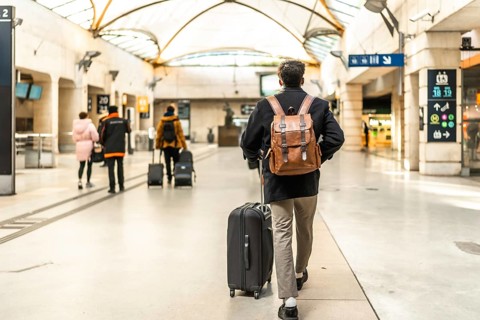 Businessman walking through a modern train station, pulling a suitcase and wearing a backpack,