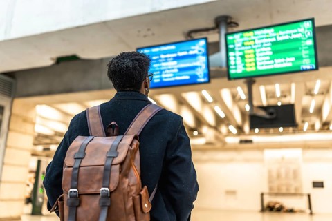 Man with a backpack standing at a train station, looking at the departure boards, preparing for a