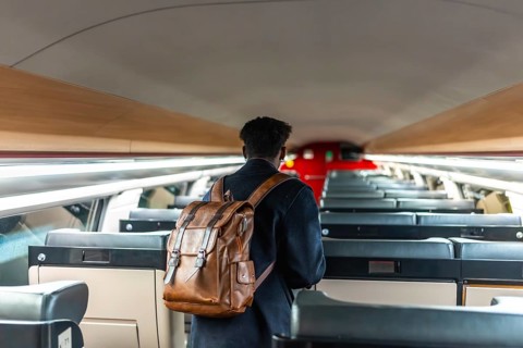 Young black man walks down an empty modern train carriage with a brown leather backpack, commuting