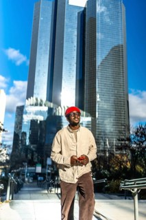 Young black man standing confidently in a modern city setting, wearing stylish casual attire and a