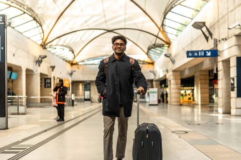 Young businessman standing on a modern train platform, smiling confidently with suitcase and