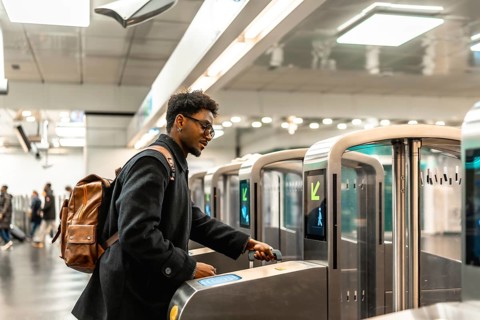 Young man with glasses and backpack tapping a contactless ticket at a modern subway turnstile,