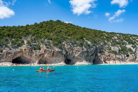 Kayakers in clear blue water, picturesque rocky coast, cliffs and Cala Luna beach, Golfo di Orosei,